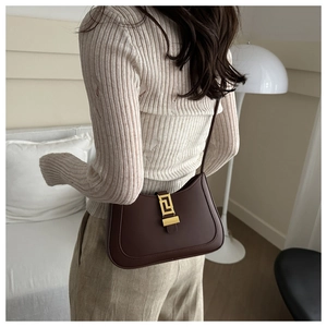 Detail of a dark brown leather shoulder bag with a vintage gold buckle on a model