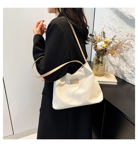 Détail de la texture du sac en toile crème avec logo en cuir sur fond de blazer noir