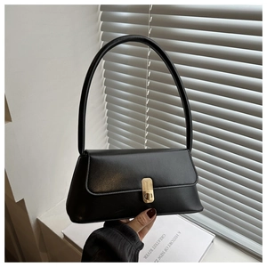 Detail of minimalist black baguette bag with gold twist lock and smooth leather texture