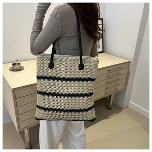 Detail showing woven straw tote bag with black stripes and secure zipper closure