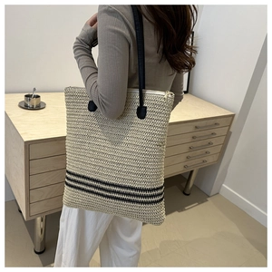 Detail of striped straw tote bag showing handwoven texture and black leather shoulder straps