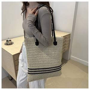 Detail of hand-woven straw bucket bag with black stripes and leather shoulder straps