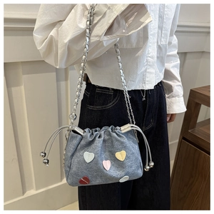 Detail of light blue denim bucket bag with colorful heart patches and silver chain strap