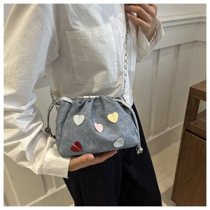 Detail of blue denim bucket bag with colorful heart patches and silver chain strap