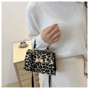 Detail of leopard print fabric handbag with gold twist lock on a wooden cabinet background