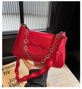 Close-up of red leather handbag with elegant bow detail and floral metal chain link