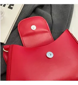 Detail of red leather crossbody bag featuring a shiny finish and silver magnetic snap closure