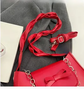 Detail of red synthetic leather shoulder bag featuring a woven handle and bow decoration