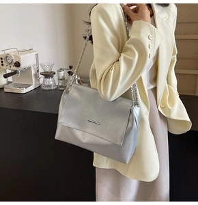 Détail du sac bandoulière argenté métallisé avec chaîne porté sur un blazer jaune
