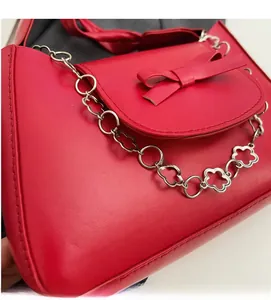 Detail of red leather shoulder bag featuring bow decoration and silver floral chain link