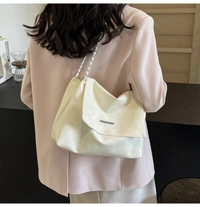 Détail d'un sac cabas beige minimaliste avec bandoulière chaîne argentée porté à l'épaule