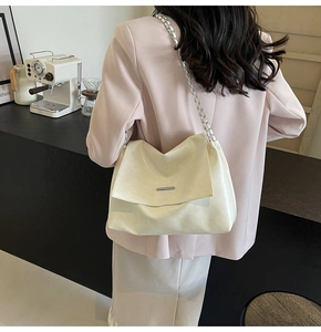 Gros plan d'un sac sous les bras en cuir crème avec barre métallique et bandoulière chaîne