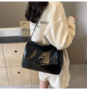 Détail du sac à rabat en cuir noir brillant avec bandoulière chaîne argentée sur modèle