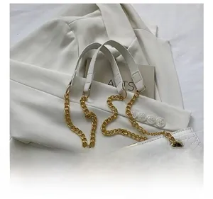 Detail of white crocodile pattern tote with gold chain strap on a white blazer