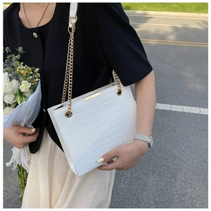 Detail of white crocodile pattern tote bag with gold chain strap on street background