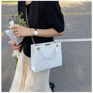 Detailed view of crocodile pattern tote with gold chain strap held in a street setting