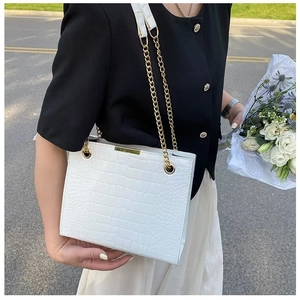 Elegant white crocodile embossed tote bag with gold chain strap held by a model outdoors