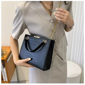 Detail of black crocodile texture tote bag with elegant gold chain strap and metal trim