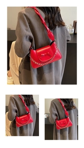 Detail of red crossbody bag with twisted strap, ribbon bow, and delicate gold chain link