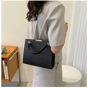Detail view of black crocodile pattern tote with gold chain strap on a model shoulder