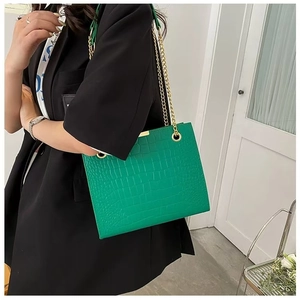 Detail of green crocodile texture shoulder bag with gold chain strap worn by a model