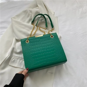 Detail of emerald green crocodile embossed tote bag with gold chain strap on white blazer