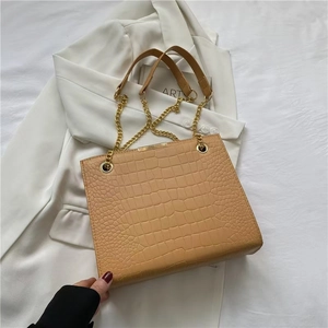 Close-up of light brown crocodile pattern PU leather with elegant gold chain and strap