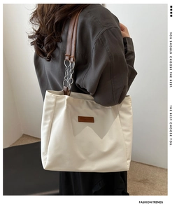 Detail of a large cream tote bag featuring brown straps with silver chain accents