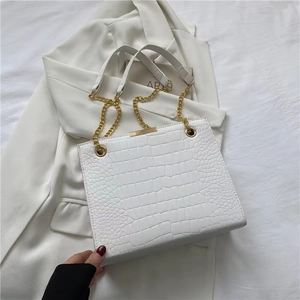 Detail of white crocodile embossed leather tote bag with gold chain strap and metal trim