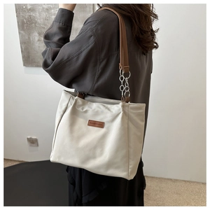 Detail of beige tote bag with brown leather strap and silver chain link accents