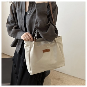 Model wearing minimalist beige canvas tote bag with brown leather straps and silver chains