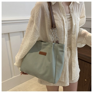 Close-up of light green canvas tote with brown leather strap and metal chain detail