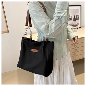 Detail of black tote bag featuring brown leather strap and silver metal chain link