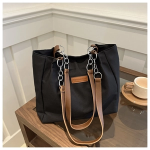 Detail of black canvas tote bag with brown leather straps and silver chain accents