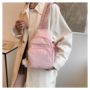 Detailed side view of a pink nylon crossbody chest bag with a white plush pompom charm