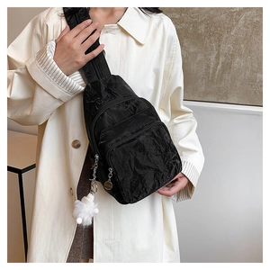Detail of black pleated chest bag with multi-zipper pockets and white pompom charm