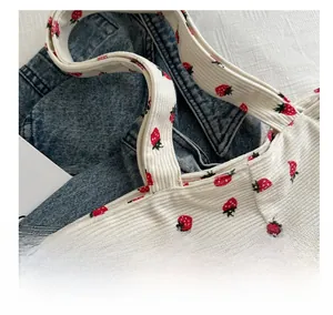 Close-up of white corduroy tote bag featuring red strawberry print and handle stitching