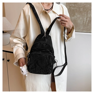 Detail of black pleated nylon crossbody bag featuring a soft white lamb plush charm