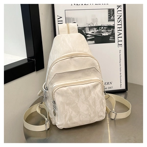 Detail of cream-white sling bag showing pleated texture and multi-pocket design