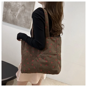 Détail d'un sac cabas en velours côtelé marron avec broderies de fraises rouges et anses