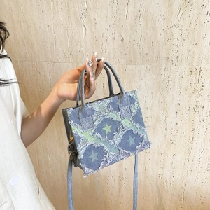 Blue denim mini tote bag with green star print and frayed edges shown in hand