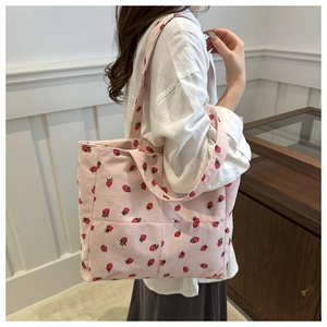 Detail of pink corduroy tote bag with strawberry pattern shown on shoulder