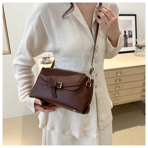 Detail of a dark brown vintage crossbody bag with belt buckle on a stylish model