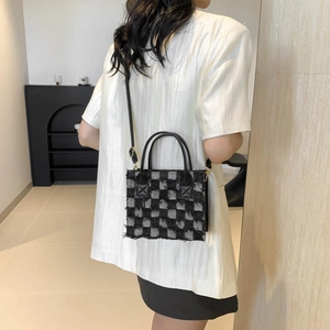 Checkerboard denim handbag with fringe trim and leather handles in a modern setting