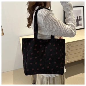 Sac fourre-tout en velours côtelé noir à motif fraises porté par un mannequin en intérieur