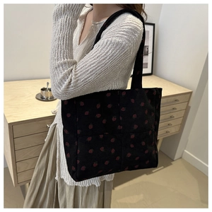 Detail of black corduroy tote bag with red strawberry embroidery and ribbed texture