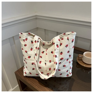 Vue détaillée du cabas en velours côtelé crème avec motif fraises sur table en bois