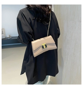 Détail d'un petit sac beige à chaîne avec boucle en T dorée porté par un mannequin