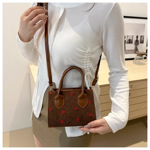 Brown corduroy crossbody bag with red strawberry pattern shown on a model