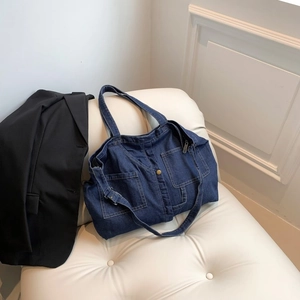 Detail of dark blue denim tote bag with visible stitching and metal buckle on a chair